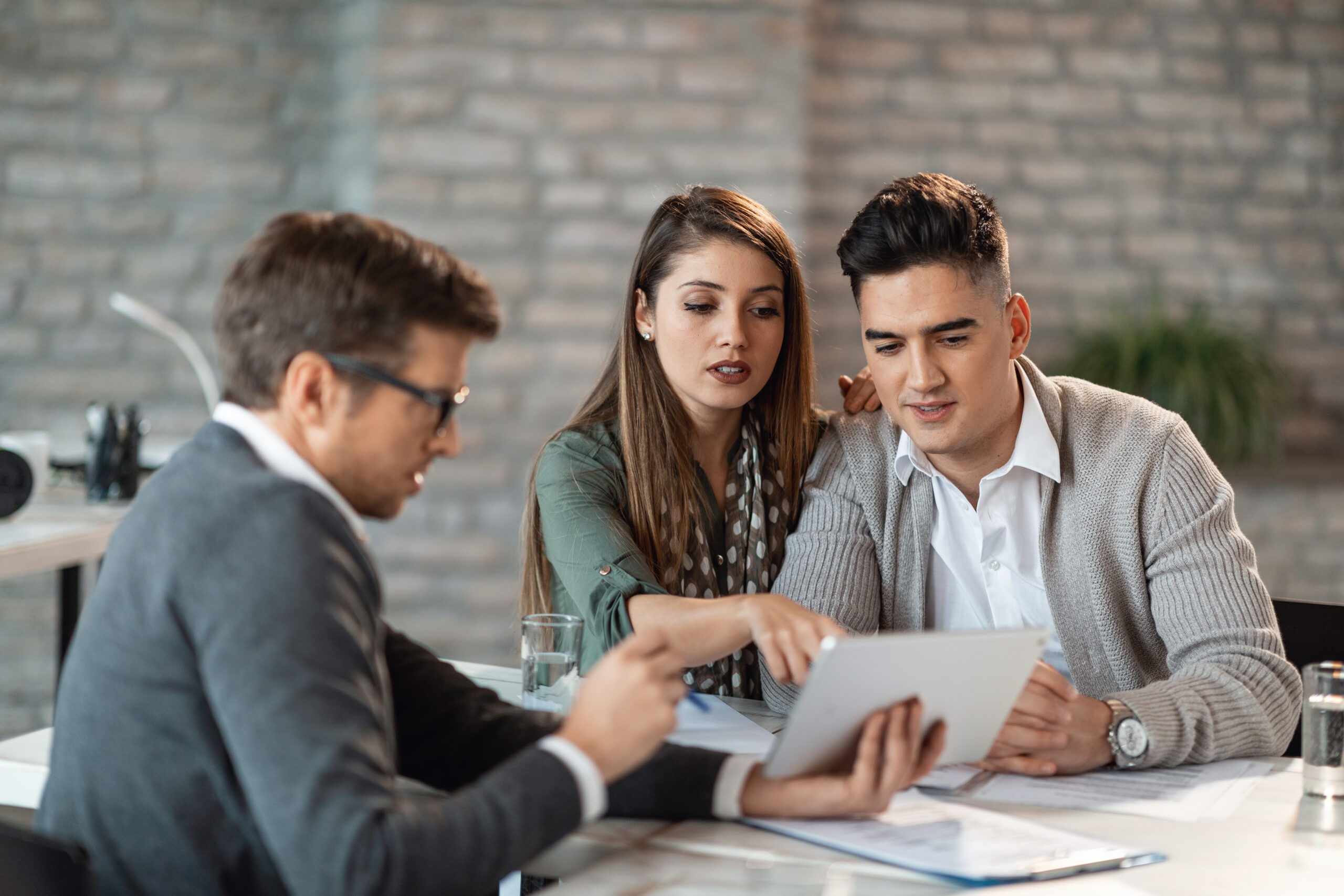 Young couple using touchpad with insurance agent and while making loan repayment plan during a meeting.