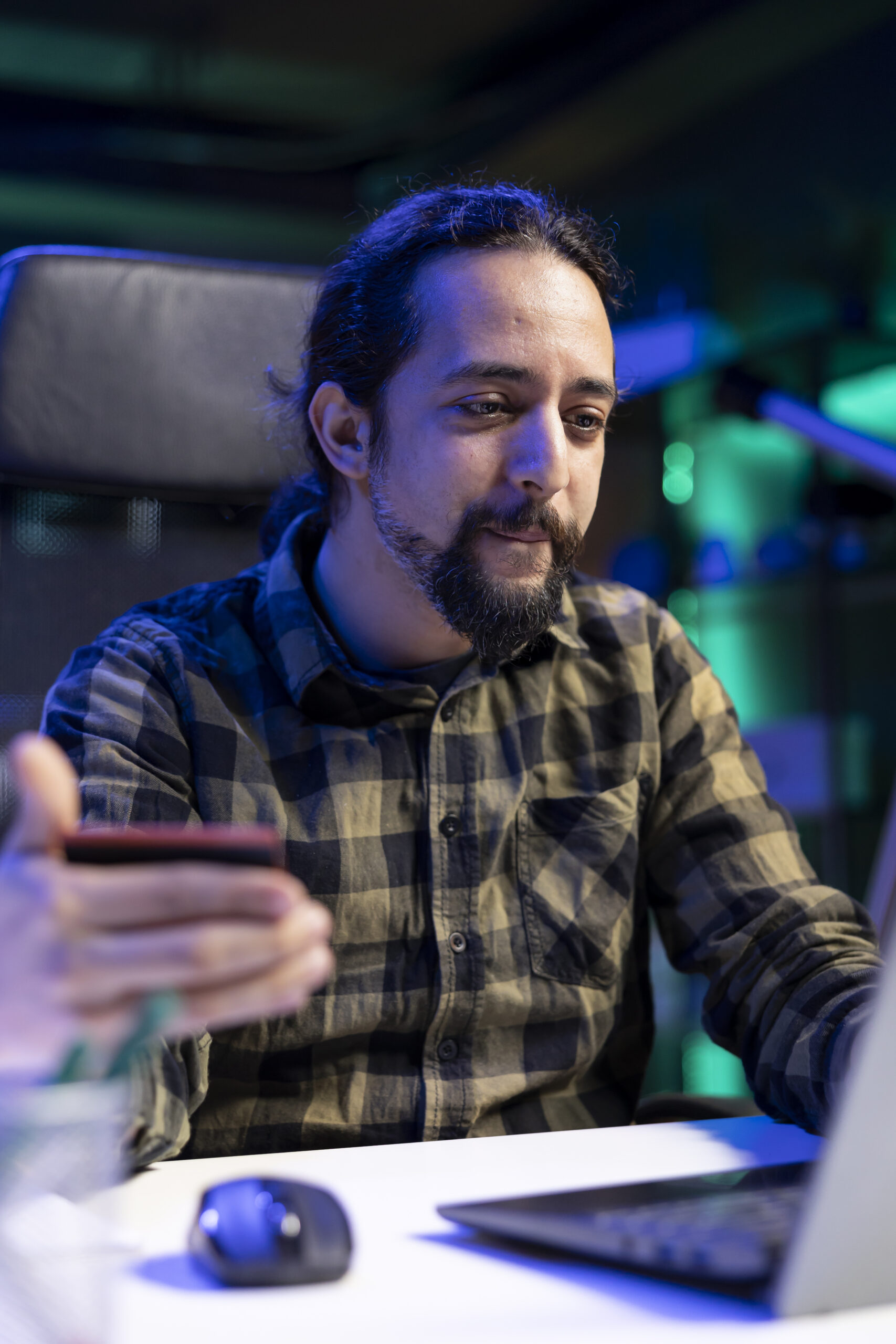 Male individual with credit card, purchasing in an online store making wireless payments at home. Young bearded man using laptop to buy and pay for products. Electronic shopping concept.